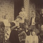 Sepia photo of ten men and women standing on the front porch of McCrae House. Some of them are sitting, but most of them in standing.