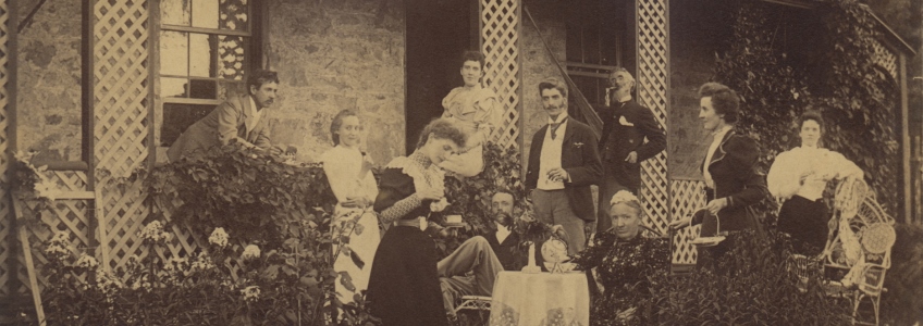 Sepia photo of ten men and women standing on the front porch of McCrae House. Some of them are sitting, but most of them in standing.