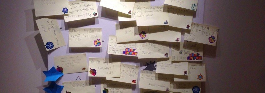 Many post its with hand written holiday memories stuck on a white wall.