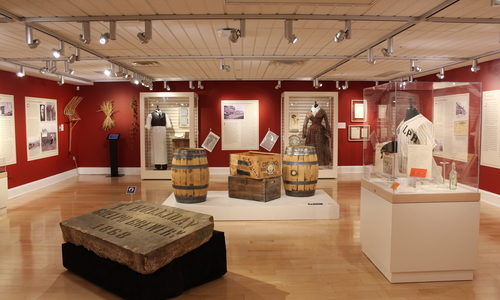 Exhibit installation view of Brewing Changes Guelph. The walls are painted red with various panels and cases around the room. A large cornerstone tablet is on display in the foreground.