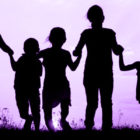 A line of silhouettes of children standing in a row. They are holding hands. Purple background.