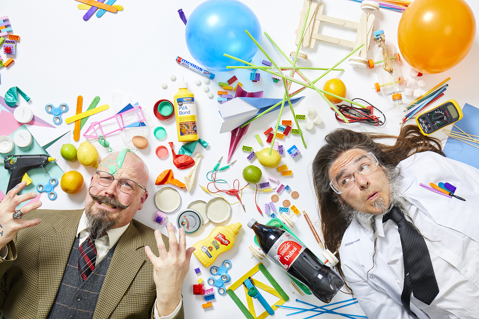 Orbax (left) and Pepper (right) laying on the ground surrounded by science experiment equipment and craft supplies.