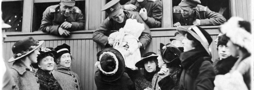 Black and white photo of First World War soldiers leaning out of a train windows and embracing loved ones below.