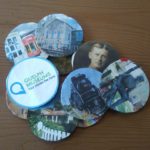 Photo of Guelph Museums themed pogs. Its a pile of 7 pogs with Guelph photos, including John McCrae, Locomotive 6167, Families Gallery, McCrae House, and the Civic Museum