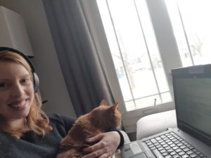 Laura Coady's work from home setup. She is holding her orange cat in her lap while sitting in front of a laptop.
