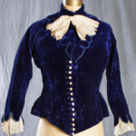 Velvet Bodice with Cravat Circa 1880 Bodice, dark blue velvet, pointed front and short 'tails' at back, sleeves cut at wrist to show embroidery and lace, 15 faux pearl buttons