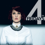 Portrait style photo of singer-songwriter Ambre McLean. She has pale skin and deep red ear length hair. She is wearing a white collared shirt with a large silver and black collared necklace. Her gaze is looking upwards above the camera.