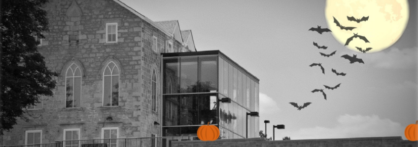 Black and white photo of the exterior of the Civic Museum. A large full moon has been photoshopped in the top right corner. A group of bats are flying over the moon. There are two small orange pumpkins sitting on the wall in front of the museum.