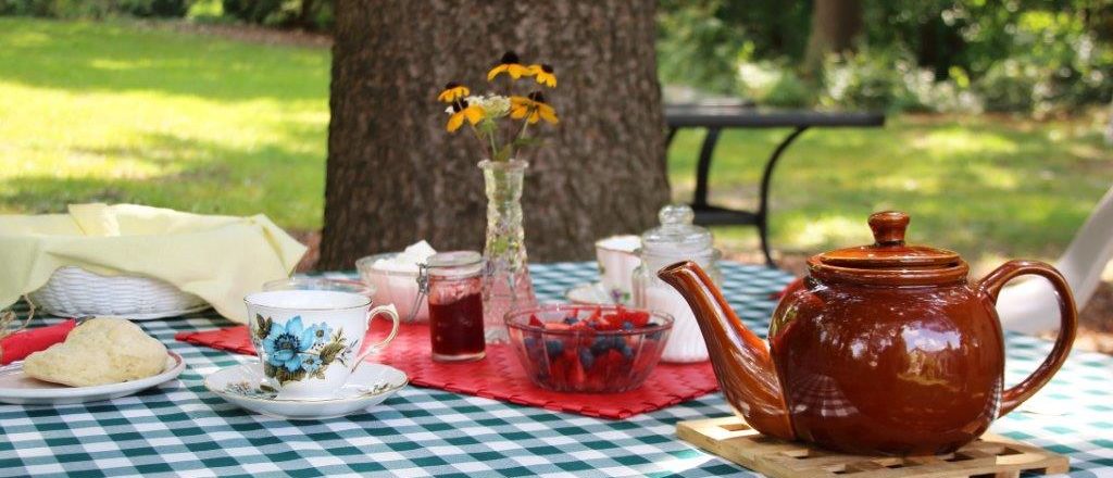McCrae House Tea at Two. A photo of a teapot. teacups, and food set up on a table outdoors.