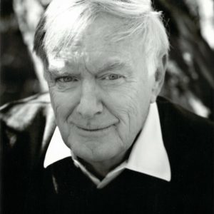 A portrait of Terry Copp in black and white. He is an older gentleman with short grey hair. He is wearing a black shirt with a white collar underneath.