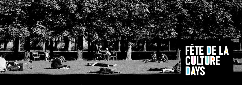 Black and white photo of people laying down on the ground in a sunny park. Trees are in the background.