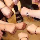 hairpipe bracelets, made by youth who took part in a workshop by Naomi Smith. Various arms are shown pointing in the center of a circle with their fists clenched. Bracelets are on their wrists.