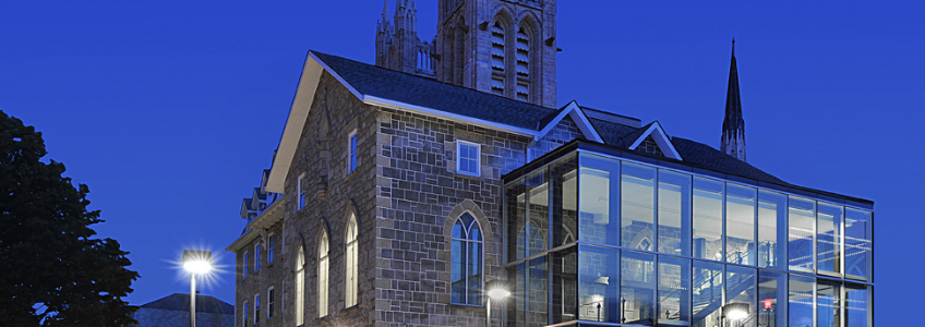 Guelph Civic Museum at nighttime. The building is illuminated by interior lights and it is dusk outside.