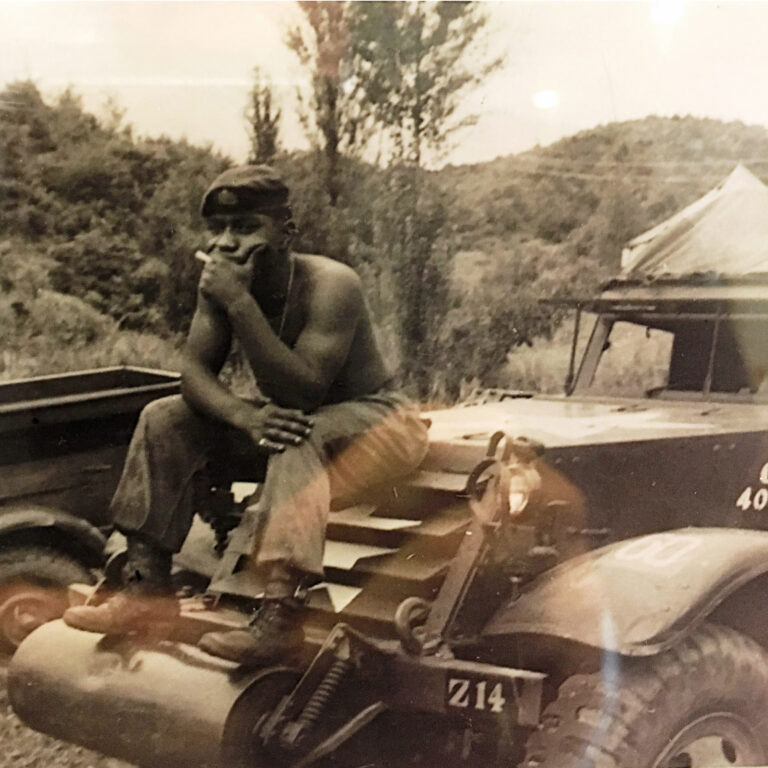 Photo of Black man in solider hat and pants, sitting on car in Korea.